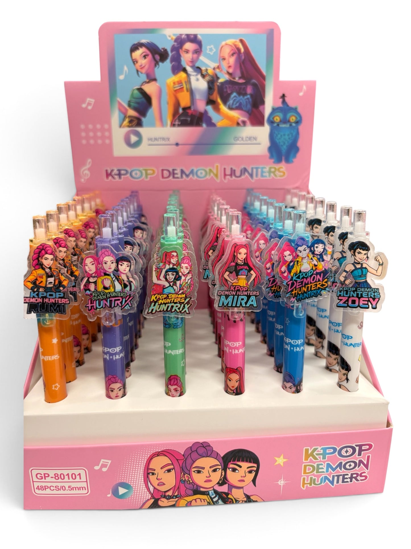 A retail display box filled with K-pop themed mechanical pencils. The display features multiple colorful pencils with character charms, including Mira, Zoe, and others from the group.
